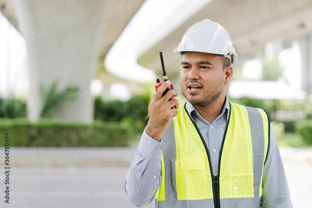 Portrait engineer handsome man or architect looking construction with the command of a radio. and white safety helmet in construction site. Portrait engineer handsome man or architect looking construction with the command of a radio. and white safety helmet in construction site.