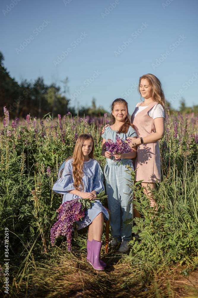 Fototapeta premium Happy mother and two little daughters play outdoors in the summer park. Family lifestyle. Mom is relaxing with the children on the green grass. 