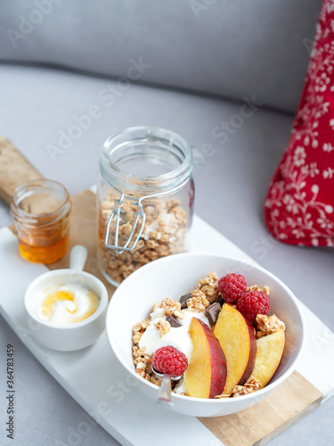Bowl of homemade granola with yogurt, honey, fresh raspberries and nectarines on a kitchen table on a sofa. Stay home Healthy breakfast.