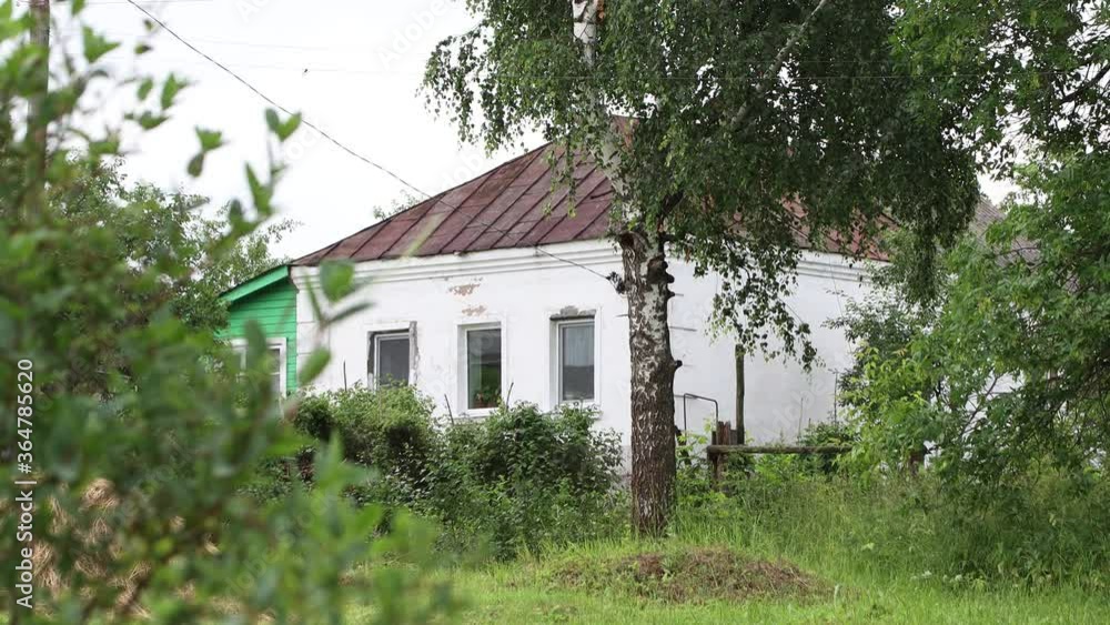The white-stone old village house is surrounded by greenery. The roof is covered with brown material. In the foreground is a green tree. 4K. The white-stone old village house is surrounded by greenery. The roof is covered with brown material. In the foreground is a green tree. 4K.
