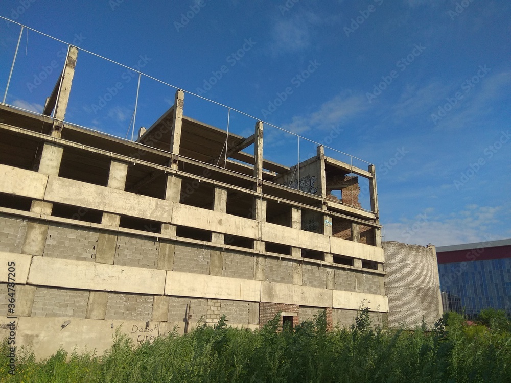 Abandoned concrete building in grey color. Unfinished constructions with the modern building on the background Abandoned concrete building in grey color. Unfinished constructions with the modern building on the background