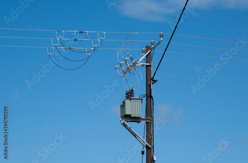 An electricity supply pylon delivering power through the UK national grid showing power cables, isolators and other equipment. Taken on a sunny day with a blue sky.