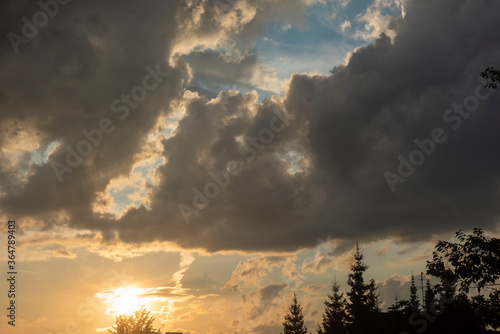 The sun at sunset over the forest bright yellow-orange colors  cumulus clouds of dark black color.