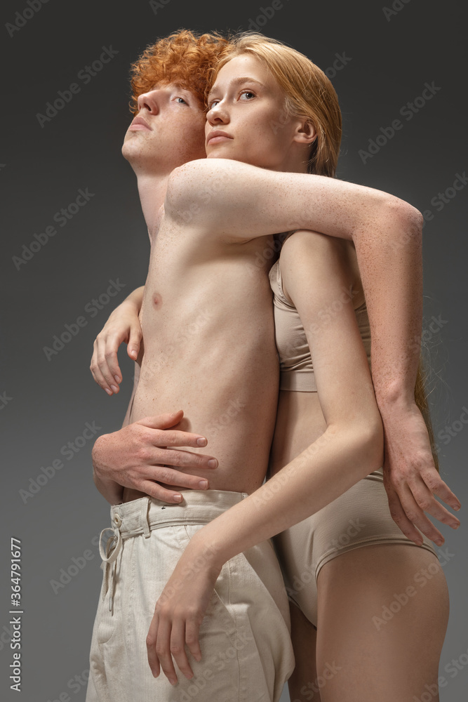 Naklejka premium Catch me. Fashion portrait of beautiful redhead couple isolated on grey studio background. Concept of beauty, skin care, fashion and style. Artwork, modern and trendy portrait. Attractive model.