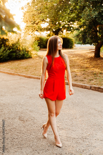 Photosession of a pretty girl walking in the city at sunset in a red dress with beautiful hair