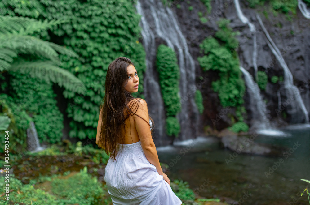Girl walks in a white dress on a background of a waterfall.