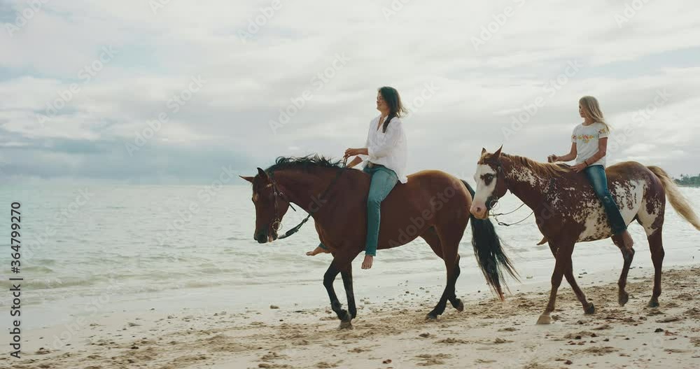 Horseback riding in sand on the beach, two friends enjoying morning ride, majestic slow motion, friendship and relaxation Horseback riding in sand on the beach, two friends enjoying morning ride, majestic slow motion, friendship and relaxation