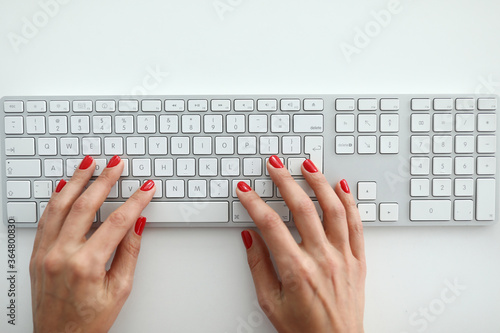 Top view of woman working on white keyboard. Female using part of computer for work. Knobs with letters. Cute fresh red nail polish. Technology and business concept