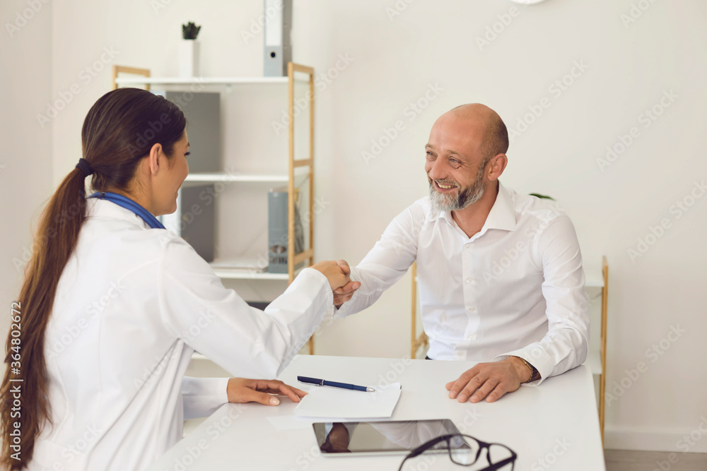 Smiling mature male patient makes doctor shaking hands at clinic office Smiling mature male patient makes doctor shaking hands at clinic office