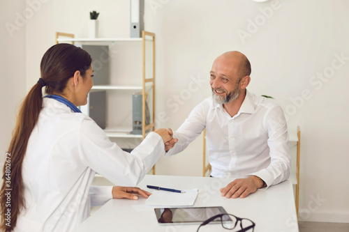 Smiling mature male patient makes doctor shaking hands at clinic office