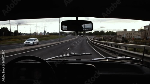 The interior of an old vintage retro AZLK Moskvich 2140 car with chrome wipers cruising on a new but bumpy bridge and highway in the city during a gray weather photo