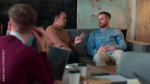 Healthy office workplace atmosphere. Two young multiethnic male business people casually chat on couch at coworking.