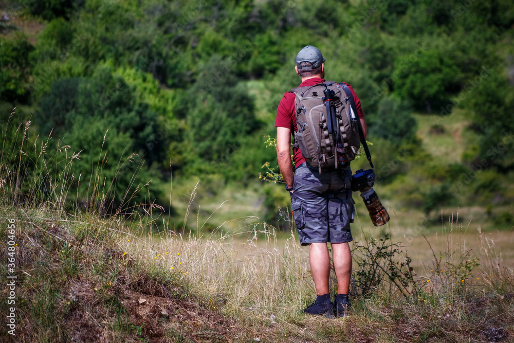 Nature photographer explores a mountain path. Mountain hiker photographer explores the area for the photographic hunting of wild animals. The man carries the backpack on his shoulders with photography