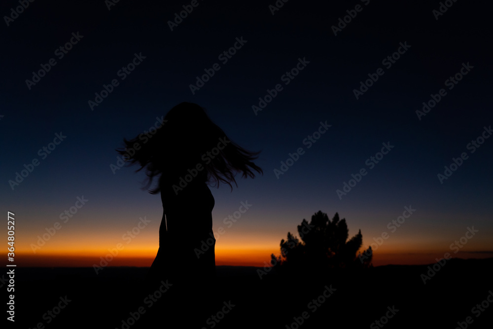 Silhouette of Young long hair woman enjoying freedom in a dramatic sunset in the mountain