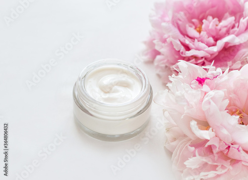 Jar of skin care cream and pink peonies