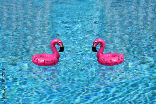 Two pink flamingo swimming rings floating toward each other in a blue pool. Concept of fun summer attraction.
