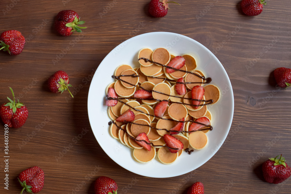 Mini pancakes with strawberries and chocolate lie on a wooden table. Mini pancakes with strawberries and chocolate lie on a wooden table.