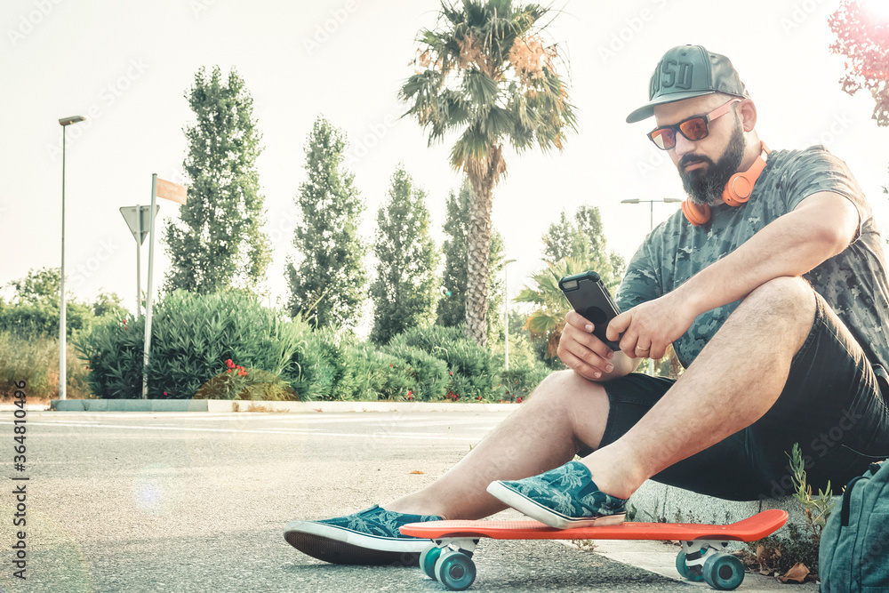 Curvy man with a skateboard answering a message with his mobile.