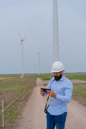 Engineer inspecting wind mill. Holding tablet.