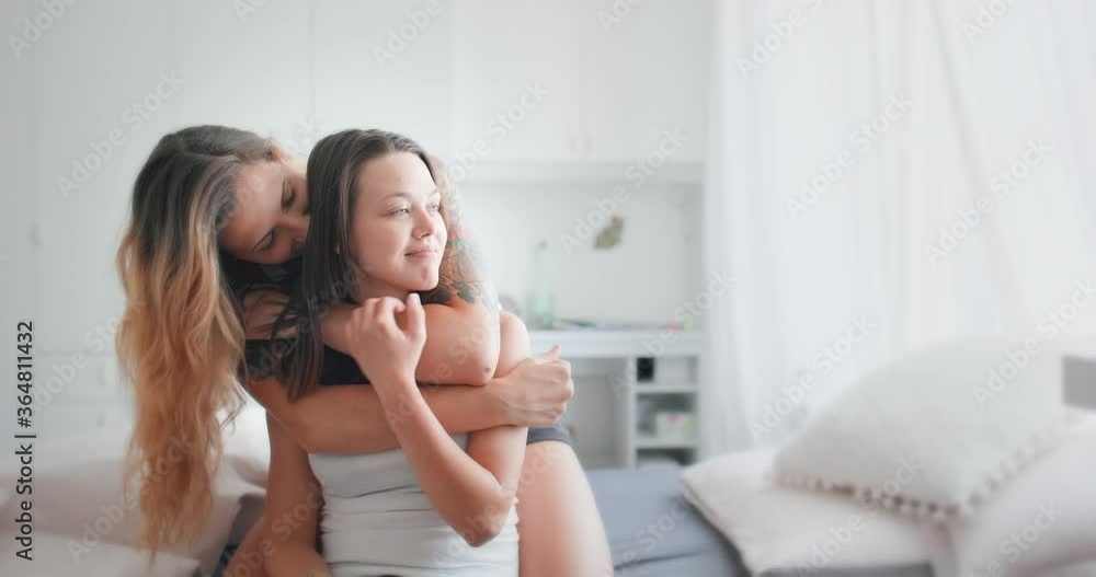 Portrait of loving lesbian couple sitting on the bed, embracing and kissing, one of them tattooed. LGBT concept.
Portrait of loving lesbian couple sitting on the bed, embracing and kissing, one of them tattooed. LGBT concept.