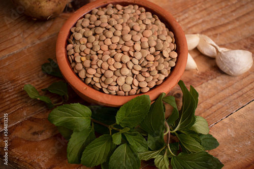 Lentils in bowl, fresh mint and garlic on wooden background