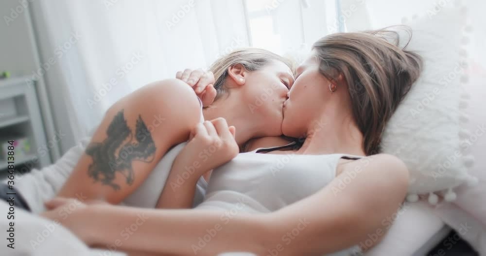 Portrait of loving lesbian couple lying on the bed and kissing, one of them tattooed. LGBT concept.
