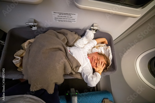 infant passenger toddler wakes up on the airplane and stretches in special baby bassinet