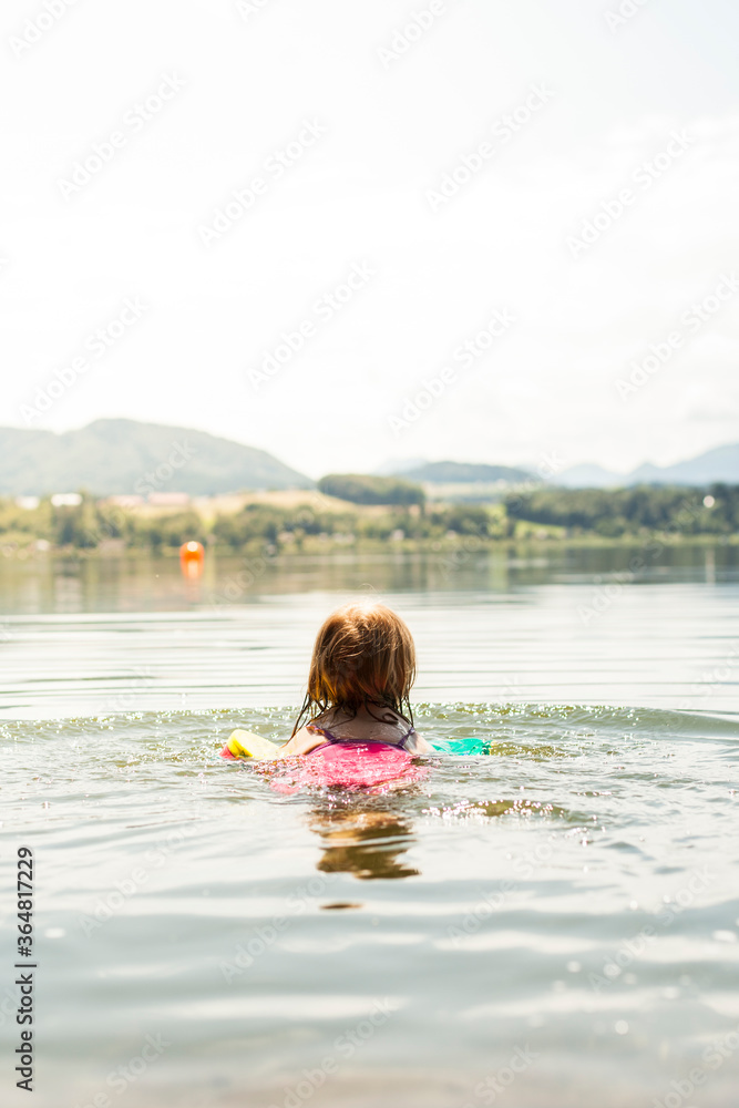Child swims with water wings in the water. Child swims in the lake. Kind schwimmt mit Schwimmflügeln im Wasser. Kind schwimmt im See.