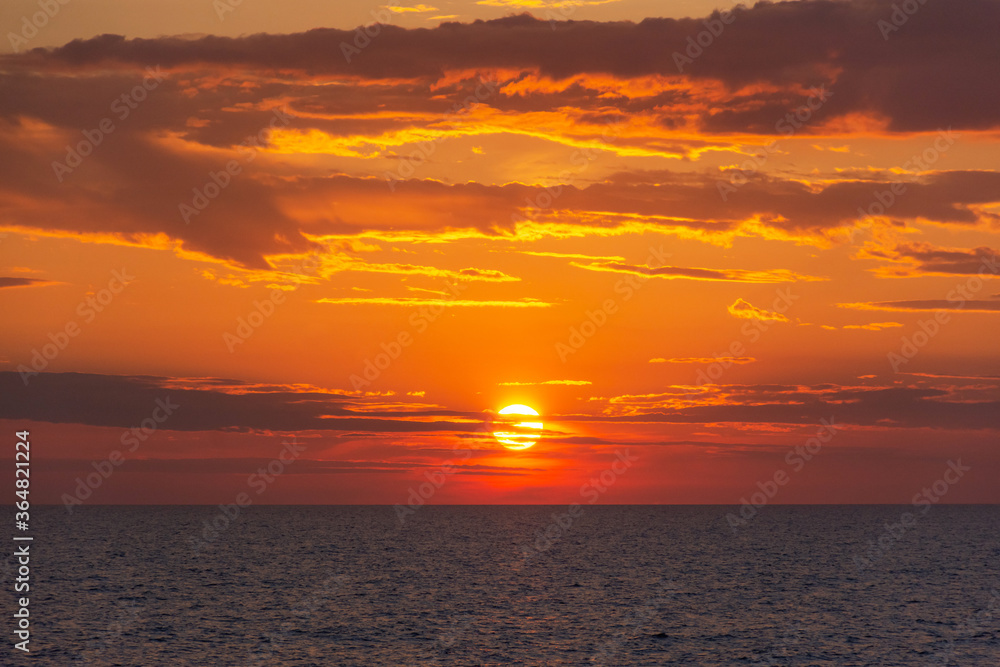 Sunset on the sea. Orange sun close - up in the clouds. Beautiful sunset sea background. Golden clouds and a huge red sun.