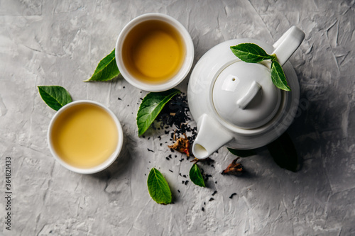 Herbal tea, cups and teapot with leaves on grey concrete background. Flat lay.