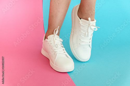 White women's sneakers dressed by a girl on a pink-blue background