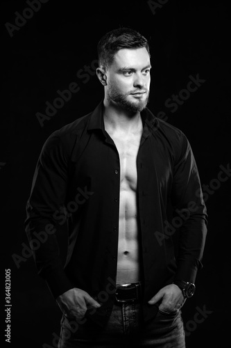 Muscular young man on dark background in fark unbuttoned shirt. Closeup. Black and white.