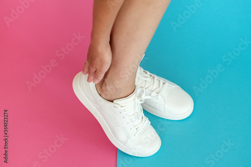 White women's sneakers dressed by a girl on a pink-blue background