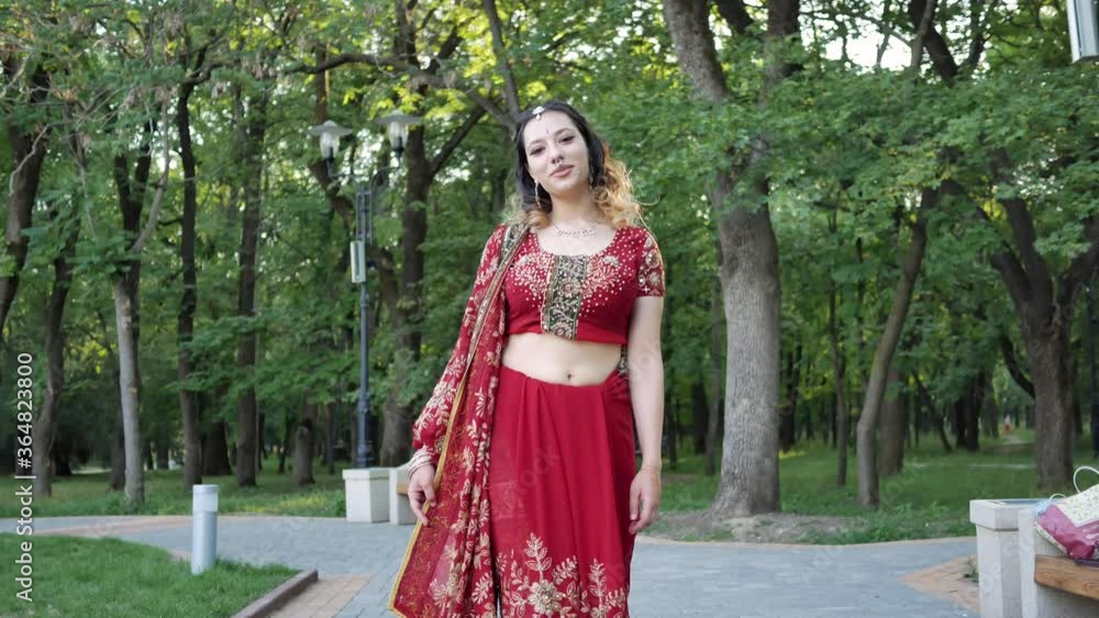 Young beautiful woman in Indian ethnic red saree walking in the Park Young beautiful woman in Indian ethnic red saree walking in the Park