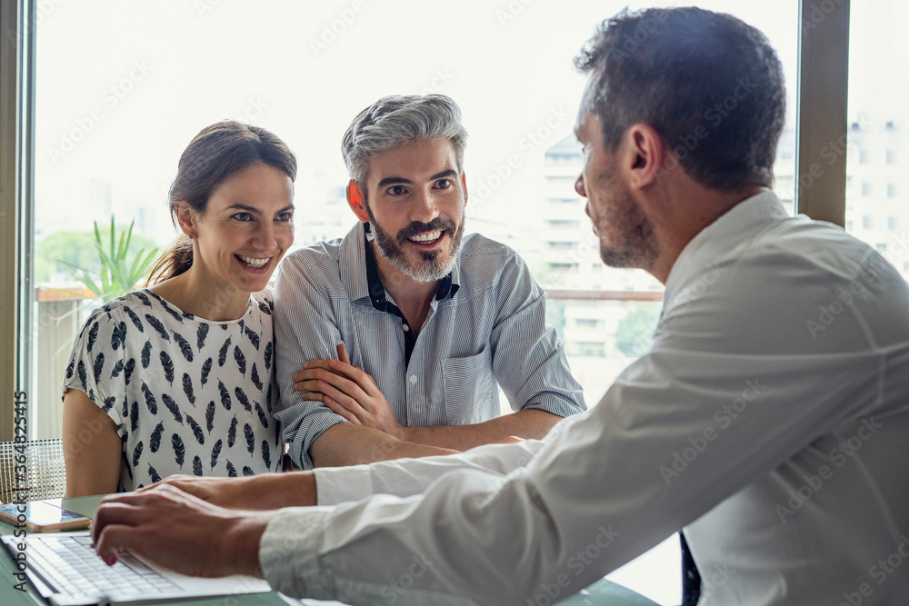 Happy couple looking at real estate agent in office Happy couple looking at real estate agent in office