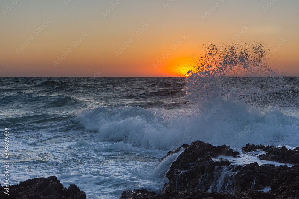Obraz premium Sunset and storm at sea. Large waves against the background of the setting sun. Summer storm on the Black sea. Beautiful sea spray on the rocks.