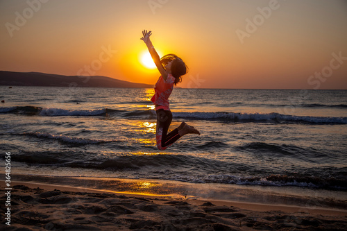 Happy young woman jumping on the beach at the sunrise. Early morning, the sun rises and shines in the sea