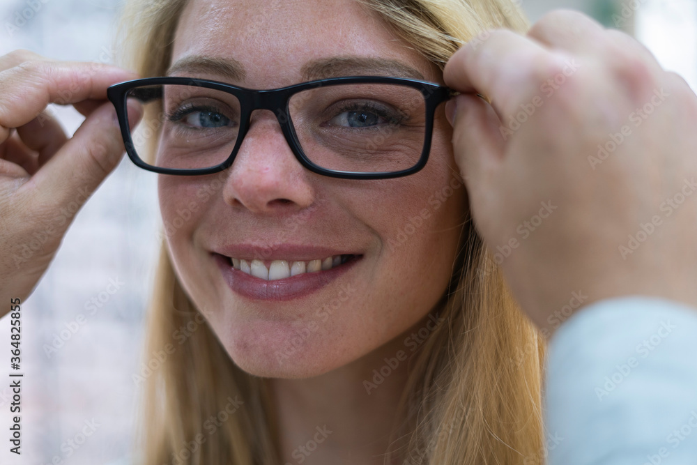 Close-up of salesperson helping customer to wear eyeglasses in store Close-up of salesperson helping customer to wear eyeglasses in store