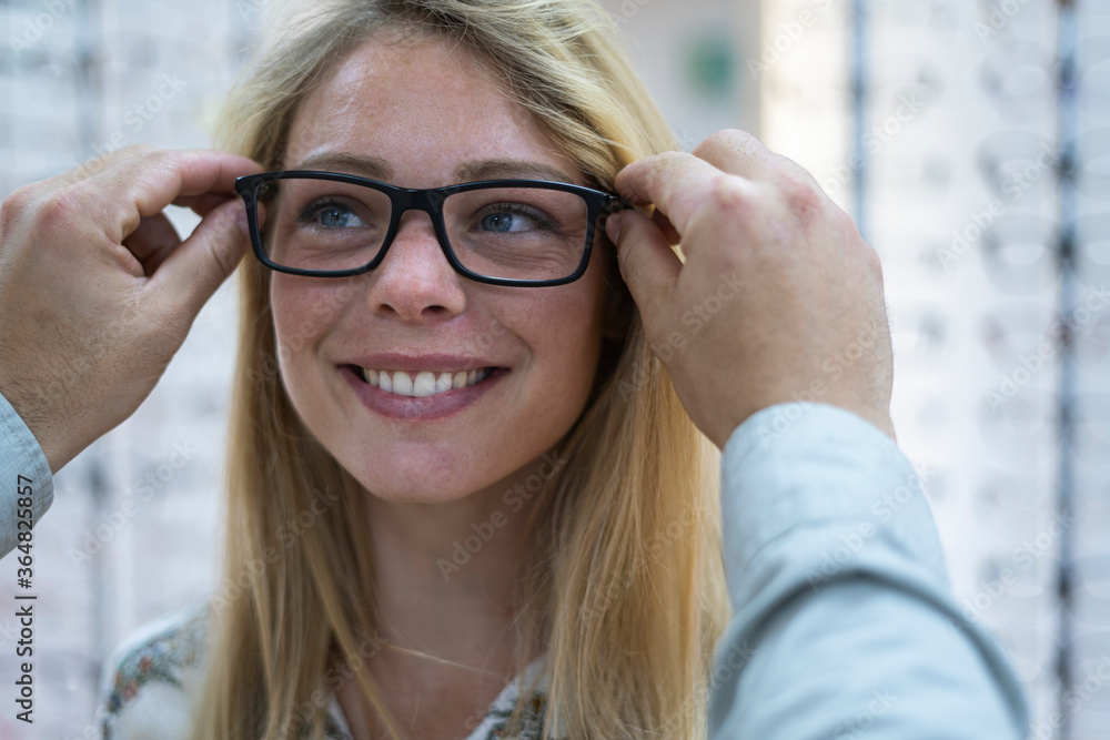 Close-up of salesperson helping customer to wear eyeglasses in store Close-up of salesperson helping customer to wear eyeglasses in store