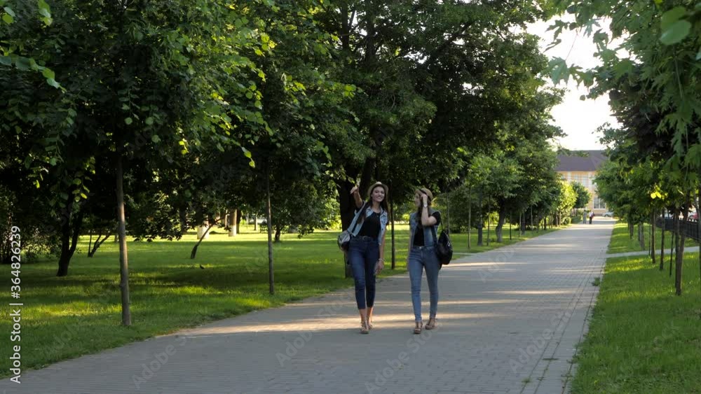 Girlfriends walk in the city Park. Stylish woman in denim suits and hats communicate and enjoy the warm summer weather. Girlfriends walk in the city Park. Stylish woman in denim suits and hats communicate and enjoy the warm summer weather.