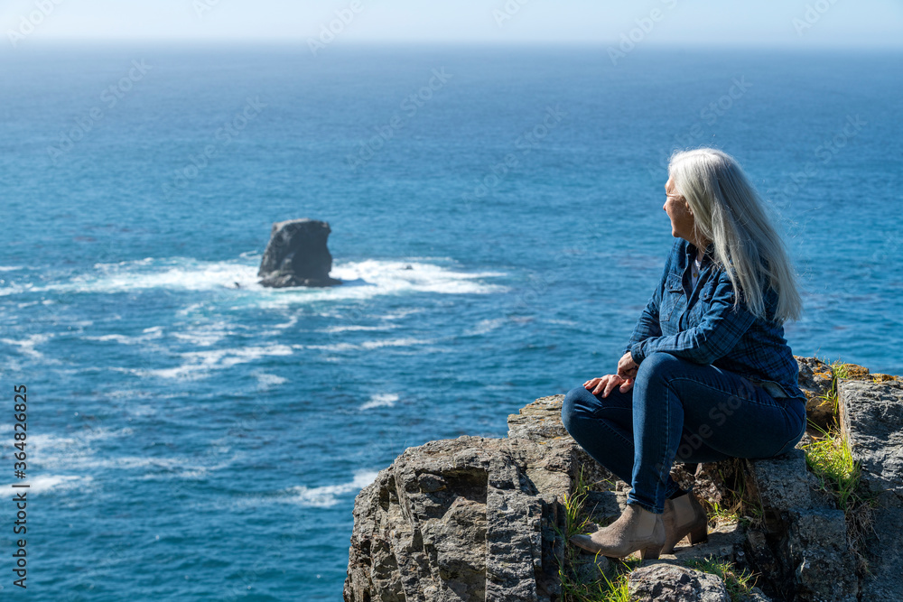 USA, California, Big Sur, Woman sitting at the edge of cliff looking at view USA, California, Big Sur, Woman sitting at the edge of cliff looking at view