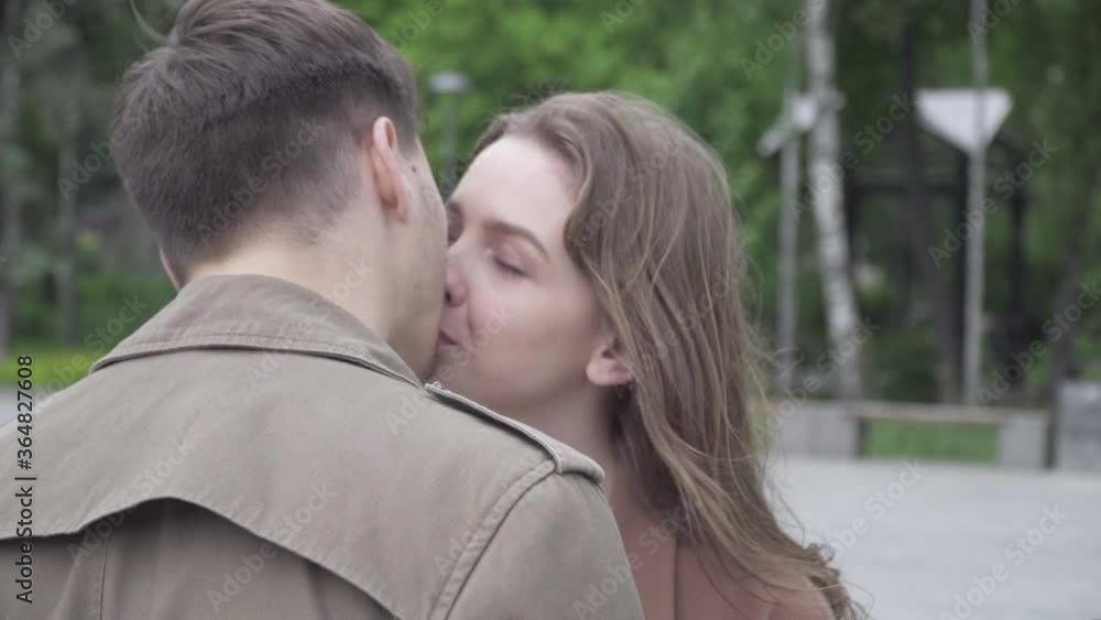 Close-up of happy smiling brunette woman looking at boyfriend with love and kissing partner. Portrait of charming beautiful Caucasian girlfriend dating with brunette man outdoors. Close-up of happy smiling brunette woman looking at boyfriend with love and kissing partner. Portrait of charming beautiful Caucasian girlfriend dating with brunette man outdoors.
