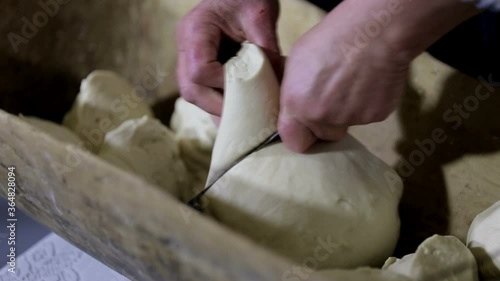 A woman cuts the dough into pieces with a knife in a wooden kneading-trough