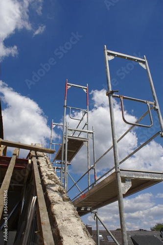 Baugerüst bei einer Dachsanierung mit braunen Dachbalken auf einer Baustelle bei blauem Himmel mit weißen Wolken