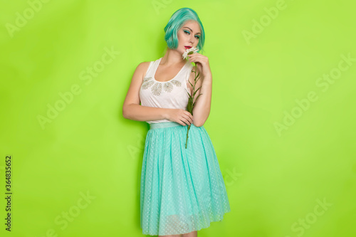 Studio portrait of beautiful mint hair feminine in white top and light blue skirt holding big chamomile in her hands,