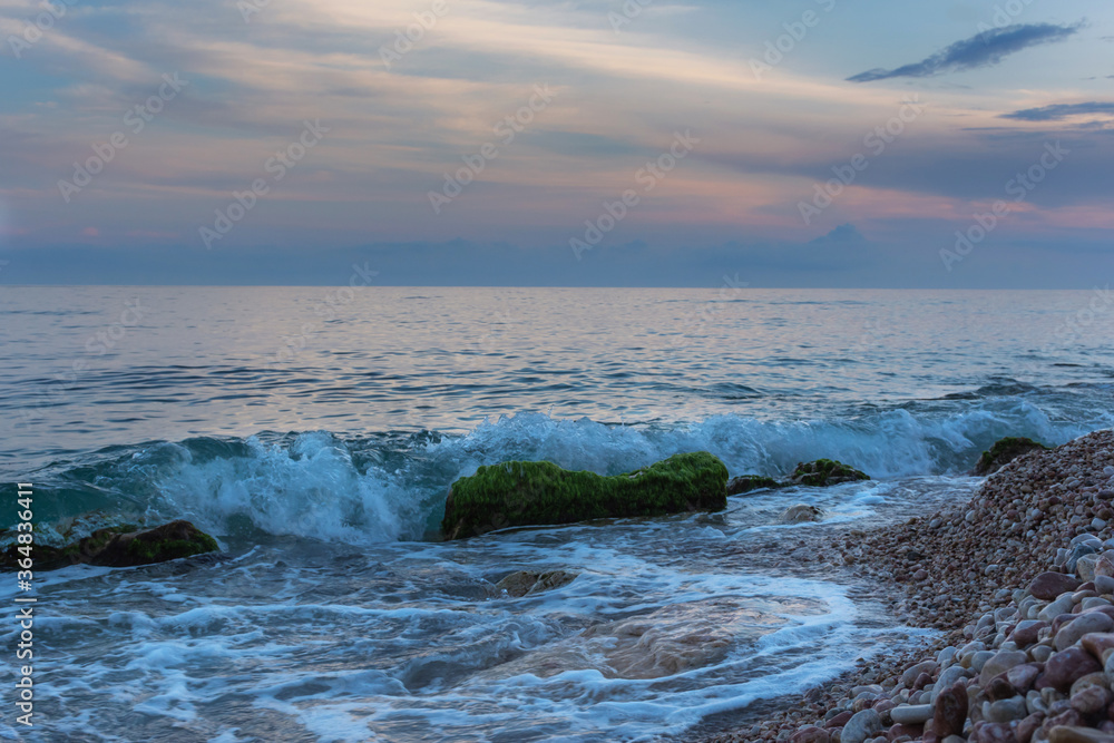 Fototapeta premium Seashore in the evening. Beautiful blue light. Landscape with pebbles in small waves. The coast of the sea without people. Relaxing sea background.