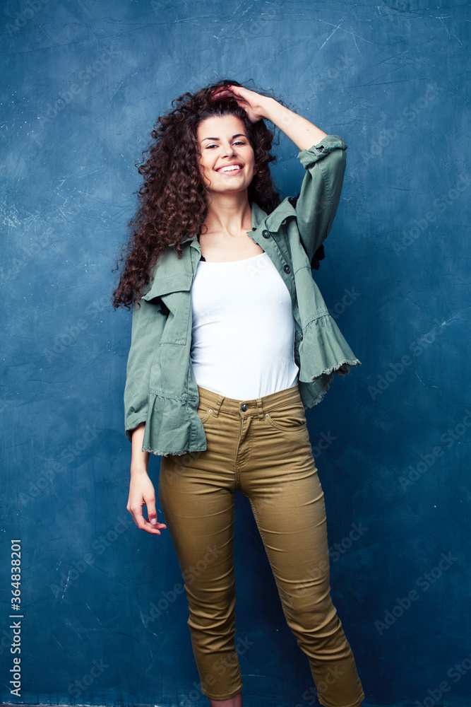 young pretty woman with curly brunette hair posing cheerful on blue background, lifestyle people concept young pretty woman with curly brunette hair posing cheerful on blue background, lifestyle people concept