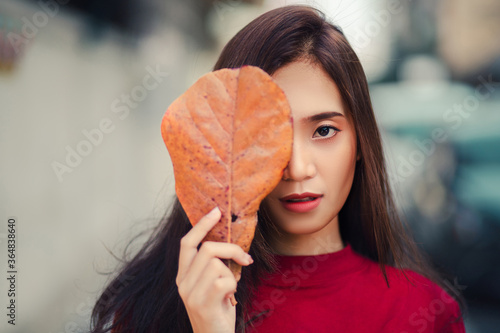 Beautiful Asian woman uses a brown leaf to cover her face. She wore bright red shirt.