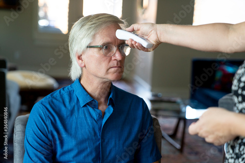 Woman checking senior man's temperature for fever with contactless thermometer