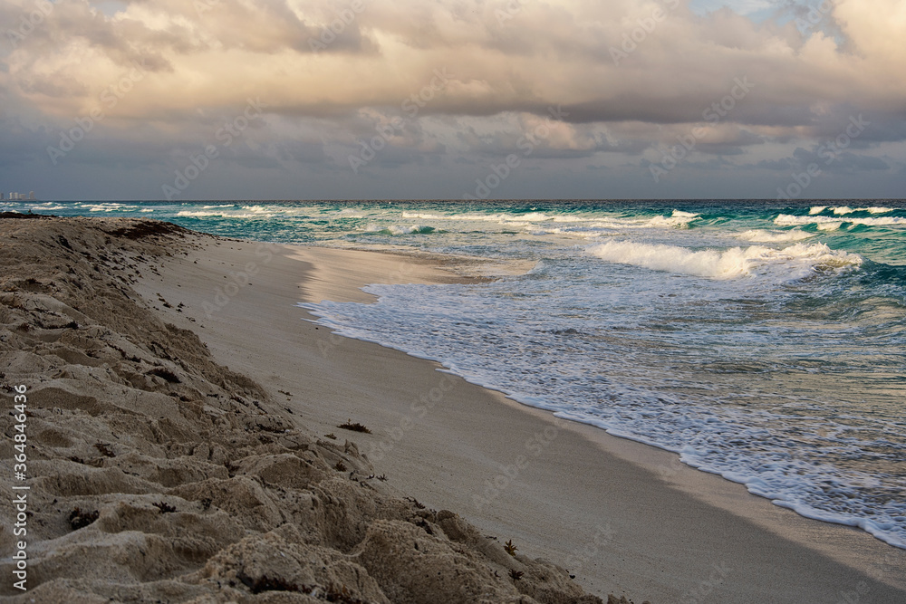 Shore beach scene with a cloudy sky and turquoise sea in Cancun, Mexico.